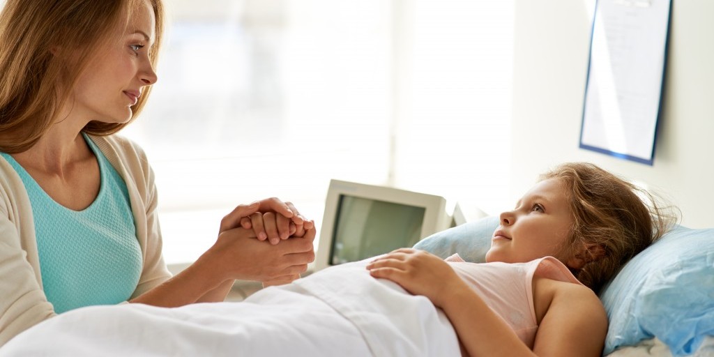 Sweet girl lying in bed in hospital with her mother near by